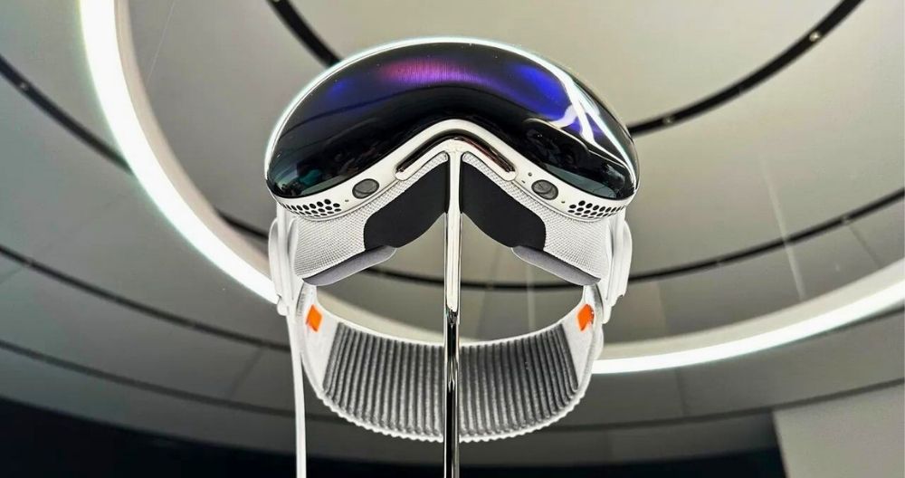 A modern Apple Vision Pro virtual reality headset is displayed in an exhibition. The headset features a sleek design with a reflective visor and white straps. 