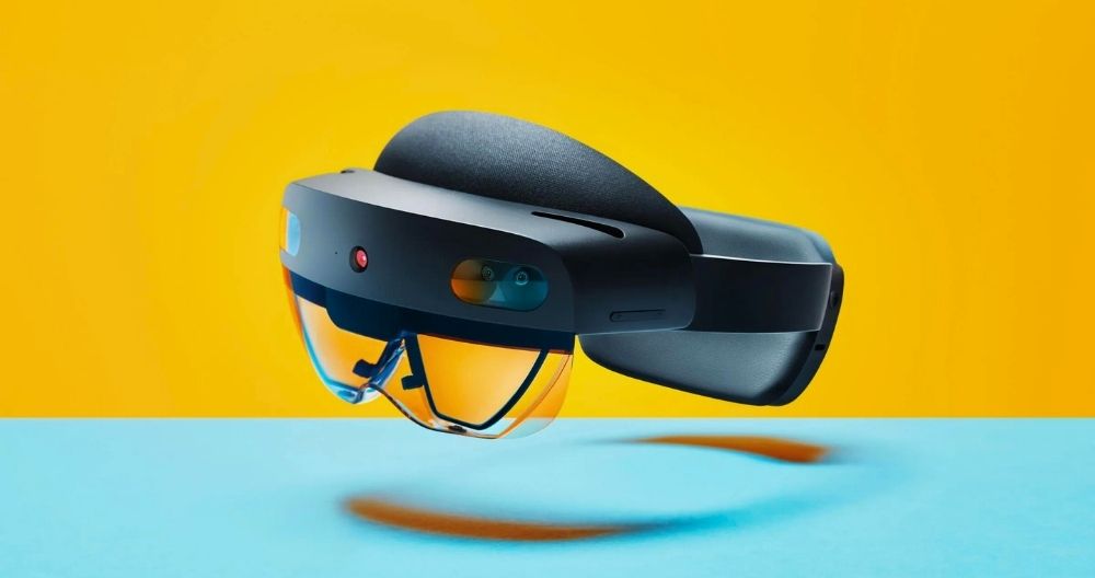 A black Microsoft HoloLens 2 mixed reality headset with visible sensors and cameras on the front, floating above a blue surface and yellow background.