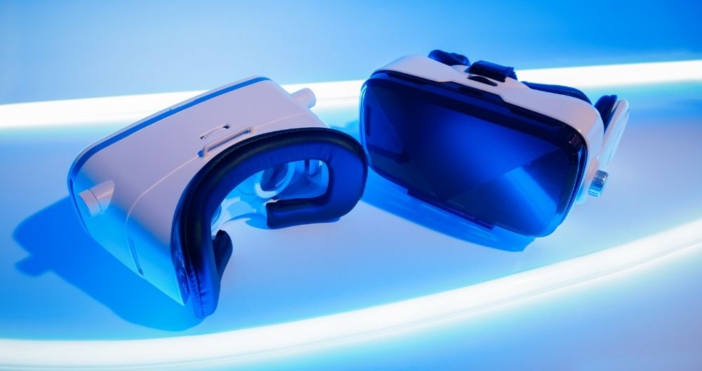 Two virtual reality headsets, one white and one black with blue lenses, are illuminated by a glowing blue light, showcasing modern technology for immersive digital experiences.