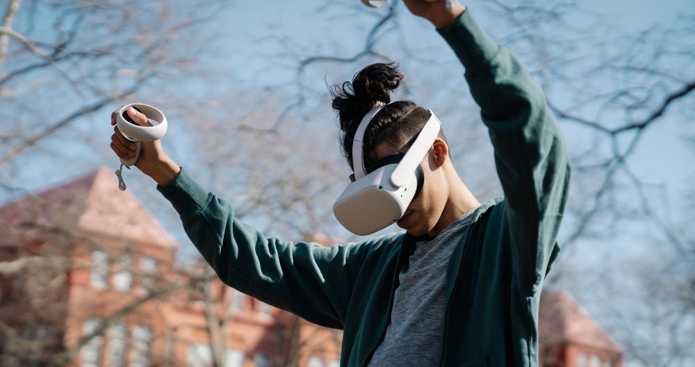 A boy wearing VR headset and enjoying it with hand controllers. The background is outdoor.
